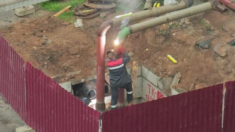 Welder works on pipe system in trench, bright sparks during joining process, Stock Footage 342922591