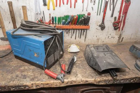 Welding machine, welding mask, and tools resting on a worn wooden workbench Stock Photos