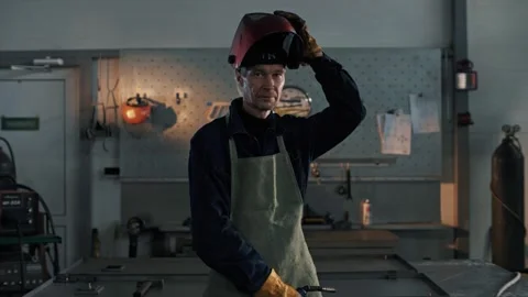 Welding shop worker looks into the camera and puts on a protective welding mask Stock Footage 265507810