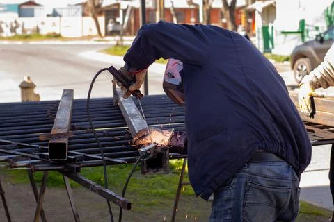 Welding torch welding a grating with a welder helmet Stockfoto's