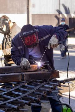 Welding torch welding a grating with a welder helmet Stockfoto's