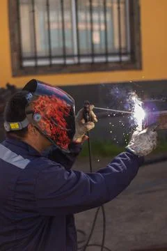 Welding torch welding a grating with a welder helmet Stockfoto's
