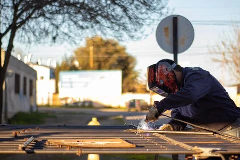 Welding torch welding a grating with a welder helmet Stockfoto's