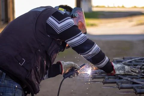 Welding torch welding a grating with a welder helmet Stock Photos