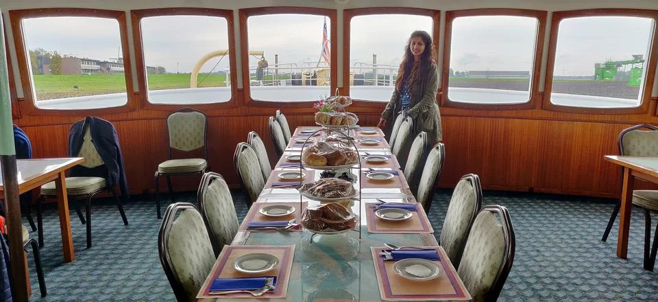 Well arranged dining table inside a ship and a woman standing besides. The view Stock Photos