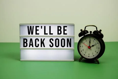 We'll Be Back Soon text on LED lightbox with alarm clock on green background Stock Photos
