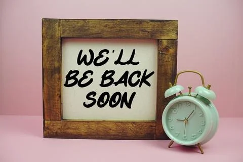 We'll Be Back Soon text with brown wooden frame and alarm clock on pink bac.. Stock Photos
