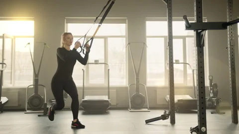 Well-built young blonde performing single leg squats on suspension trainer Stock Footage 240584863
