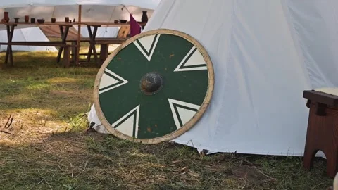 A well-crafted shield rests against a white tent in an outdoor setting during a Видео 345029704