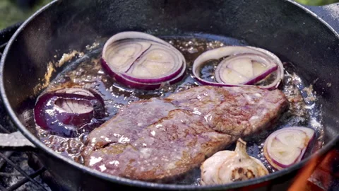 Well-done steak being cooked in a cast iron pan over coals and fire on a grill. Stock Footage 315278658