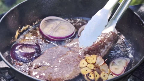 Well-done steak being cooked in a pan over coals and fire on a grill. Stock Footage 315279071
