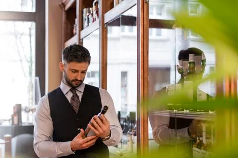 Well-dressed bartender examining whiskey bottle Stock Photos