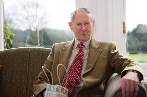 A well dressed elderly man sat in front of a bright window Stock Photos