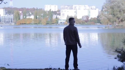 Well-dressed man skipping rocks on a river in the city. Slow motion, over the Stock Footage 81371148