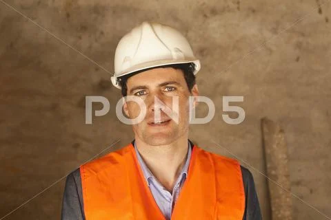 A well-dressed man wearing a hardhat and reflective vest at a building site Stock Photos