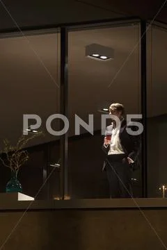 Well dressed man with wine glass looking out of apartment window. Stock Photos