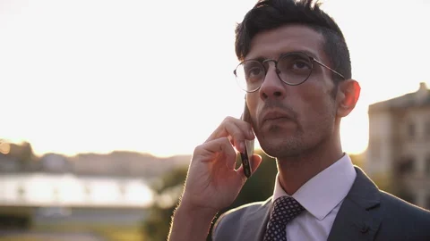 Well-dressed trendy eastern buisnessman in eyeglasses talking with mobile phone Stock Footage 110209027
