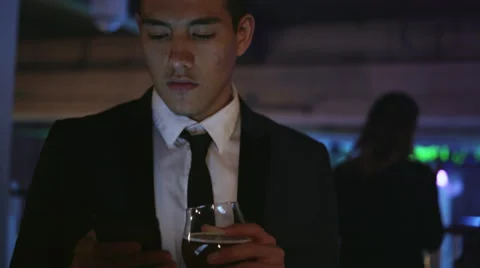 Well dressed young man in a nightclub holding a drink and texting Stock Footage