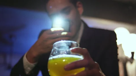 Well dressed young man in a nightclub taking a picture of his drink Stock Footage