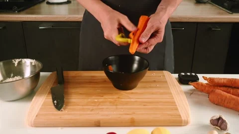 In a well-equipped kitchen, a person expertly peels fresh carrots. The wooden Video stock 316633448
