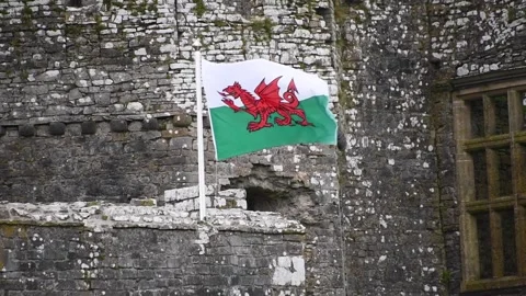 Welsh  flag flying  in the  wind against a  castle Stock Footage 272766900