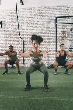 Were getting in shape and having fun doing it. a fitness group doing squats Stock Photos