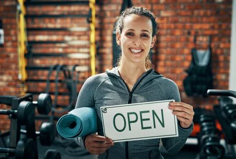 Were open and ready to get you in shape. a gym instructor holding up a open sign Stock Photos