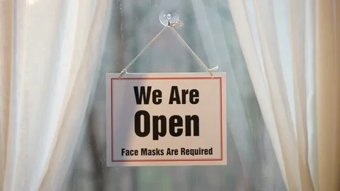 We’re Open Keep Your Distance sign swinging in the window of store front Stock Footage 143146563
