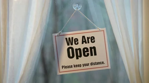 We’re Open Keep Your Distance sign swinging in the window of store front Video stock 143146573