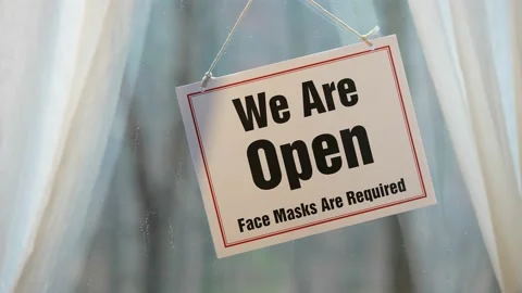 We’re Open Keep Your Distance sign swinging in the window of store front Stock Footage 143146629
