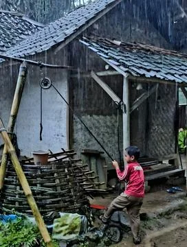 West Java Indonesia 25 August 2025 - Boy pulling water from bamboo well in rain Stock Photos