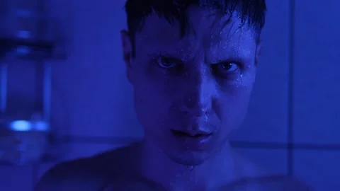 A wet man in a blue light shower stares intensely, water dripping from his face Stock Footage 304245230