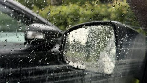 Wet reflection and heavy raindrops on a car side window with a blurred black Stock Photos