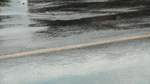 Wet road with rain falling on it puddles and vehicles cars drive over it Stock Footage 247753098