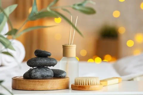 Wet spa stones with reed diffuser and massage brush on table in salon, closeu Stock Photos