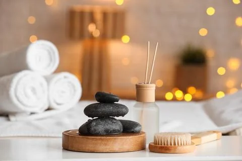 Wet spa stones with reed diffuser and massage brush on table in salon, closeu Stock Photos