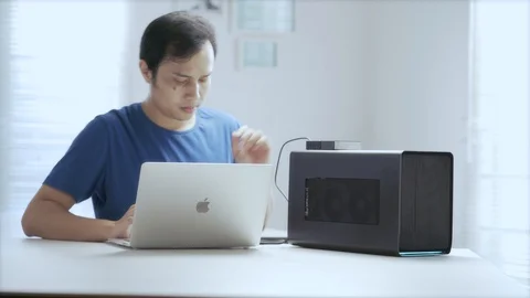 WFH Day 46-an asian young man prepares to work with the laptop, external GPU  Video stock 129727139