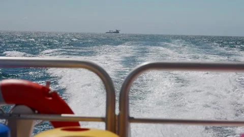 A whale watching boat, with wake waves trailing behind and a cargo ship in the Stock Footage 346491892