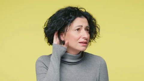 What, I cant hear you. Confused mature attractive woman having hearing problems Stock Footage 219814799