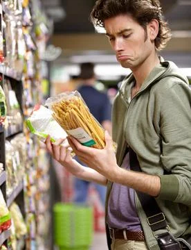 Whats the difference. A young man with two products in his hands in a grocery Stock Photos