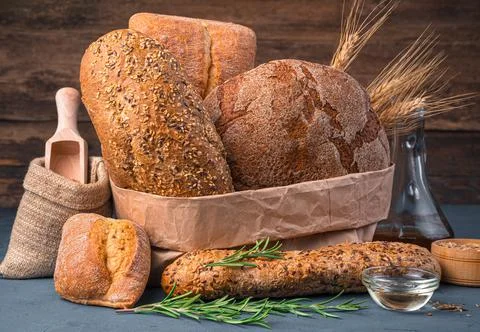 Wheat and rye bread of different types, butter and rosemary on a wooden Stock Photos