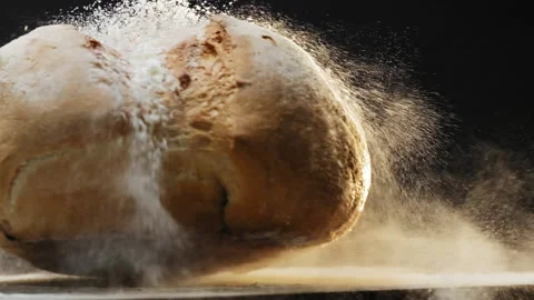 Wheat bread loaf with flour falls down onto table on black Stockbeeldmateriaal 149800475
