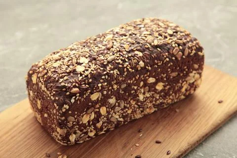 Wheat bread with mixed seeds on cutting board on grey background Stock Photos