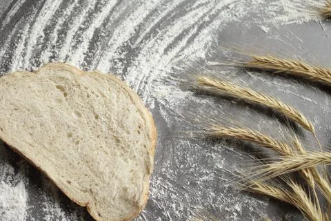 Wheat ears, a slice of bread, flour on a gray table background. View from abo Stock Photos