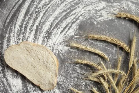 Wheat ears, a slice of bread, flour on a gray table background. View from abo Stock Photos