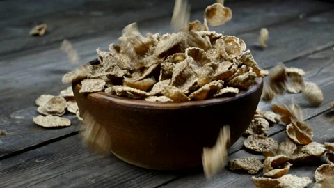 Wheat flakes fall into a clay plate on a wooden table. A bowl of dry flakes Stock Footage 143424287