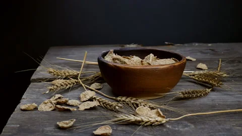 Wheat flakes fall into a clay plate on a wooden table.Healthy food Stock Footage 143429585