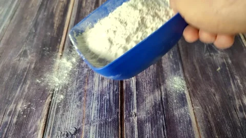 Wheat flour is poured from a blue plastic dish onto a wooden table Stock Footage 232219656