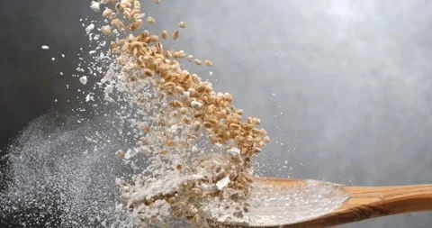 Wheat grains and flour falling from spoon creating powder cloud in slow motion Stock Footage 344849263