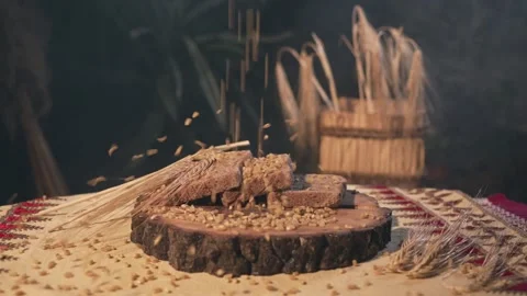 Wheat grains fall in slow motion over a wooden mat with a slice of bread Stock Footage 313927756